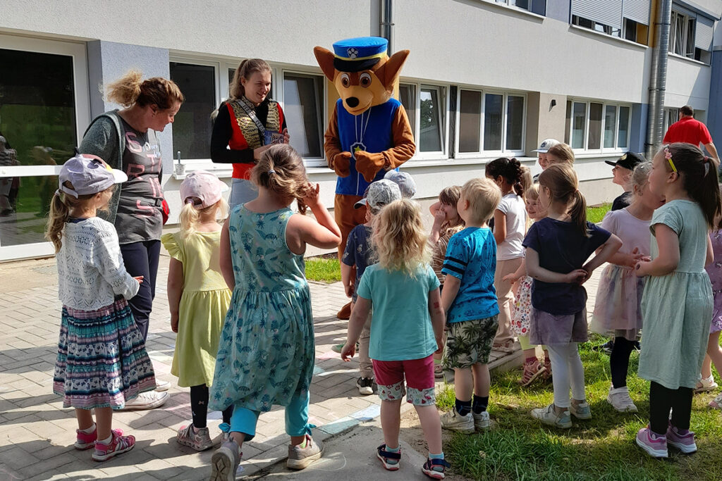 Kindergruppe mit Erwachsenen und Maskottchen im Freien