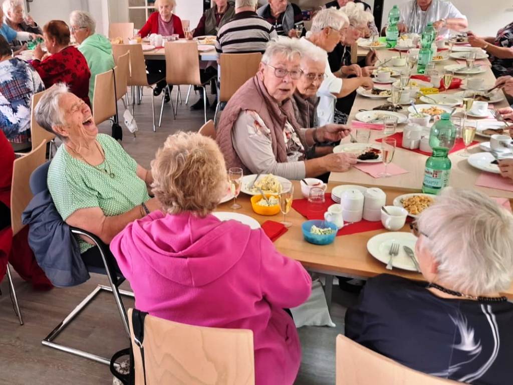 Eine Gruppe älterer Menschen sitzt fröhlich an einem langen Tisch und isst gemeinsam.