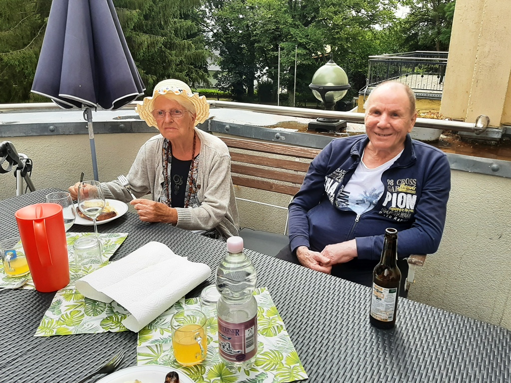 Zwei ältere Personen sitzen an einem Tisch im Freien.