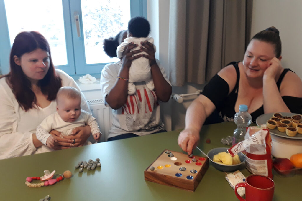 Drei Erwachsene sitzen um einen Tisch mit zwei Babys.