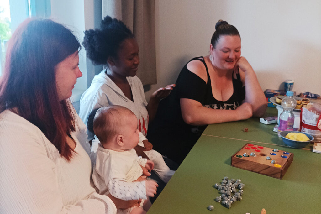 Frauen sitzen um einen Tisch, eine h&auml;lt ein Baby.