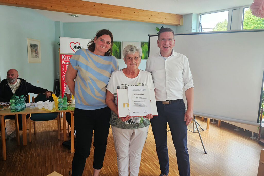 Drei Personen posieren mit einer Urkunde.