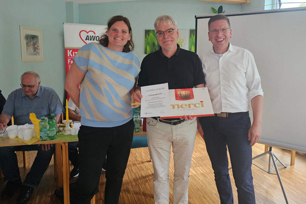 Personen stehen mit einer Urkunde vor einem AWO-Banner.