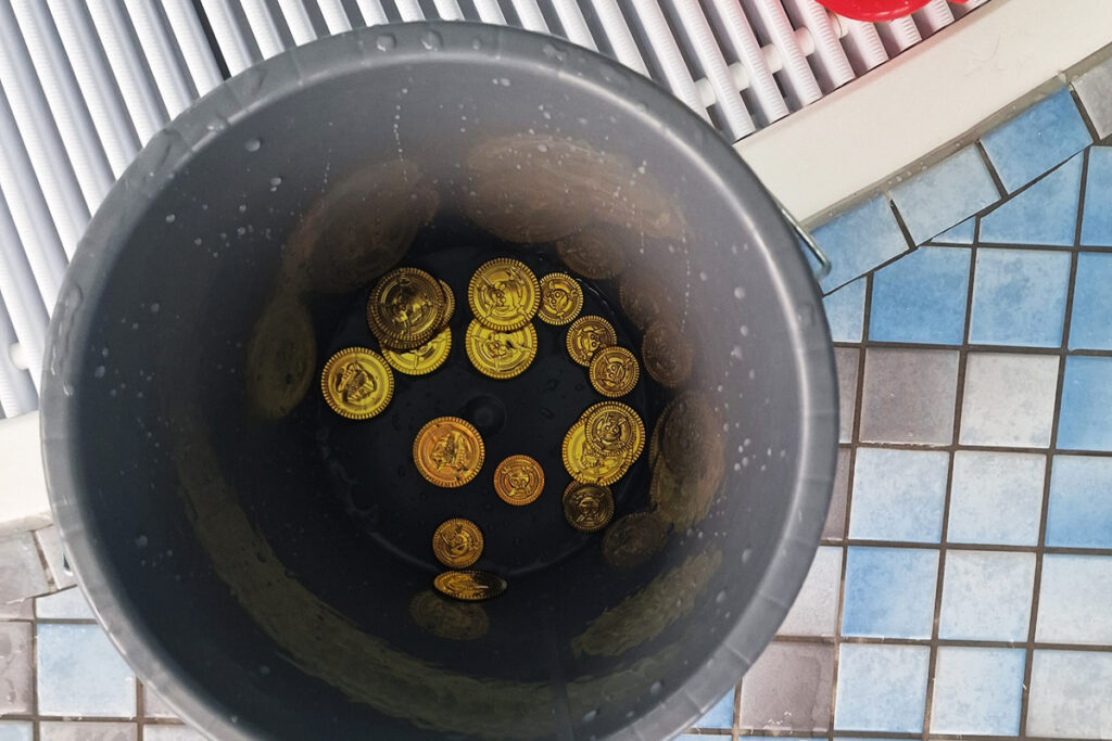 Eine graue Plastikeimer mit goldenen Spielm&uuml;nzen darin.