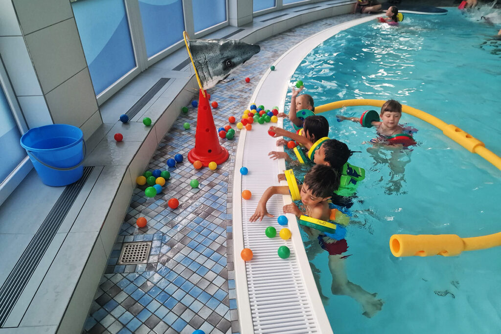 Kinder im Schwimmbad spielen mit bunten B&auml;llen.