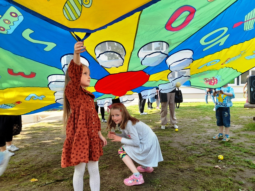 Kinder spielen unter einem bunten Fallschirm im Freien.