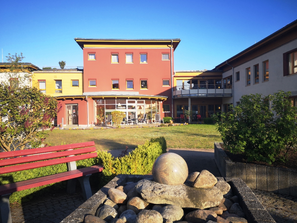 Ansicht eines modernen Gebäudekomplexes mit einem kleinen Garten im Vordergrund.