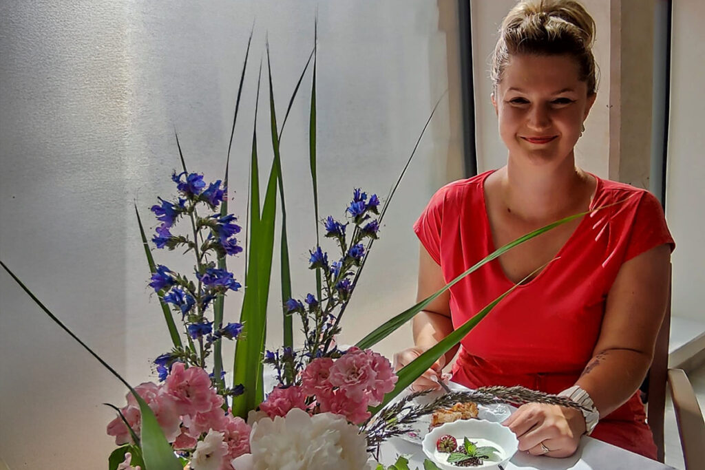 Frau in rotem Kleid sitzt an einem Tisch mit Blumen