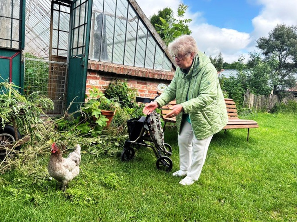 Ältere Frau im Garten mit Huhn