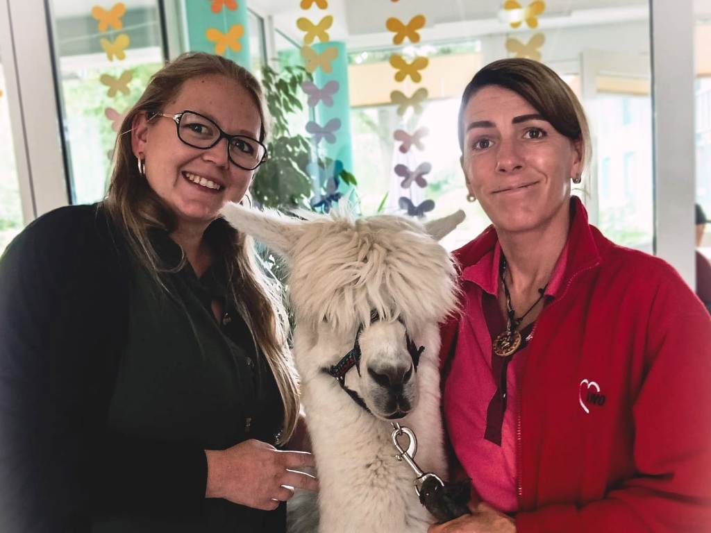 Zwei Frauen posieren mit einem Alpaka.