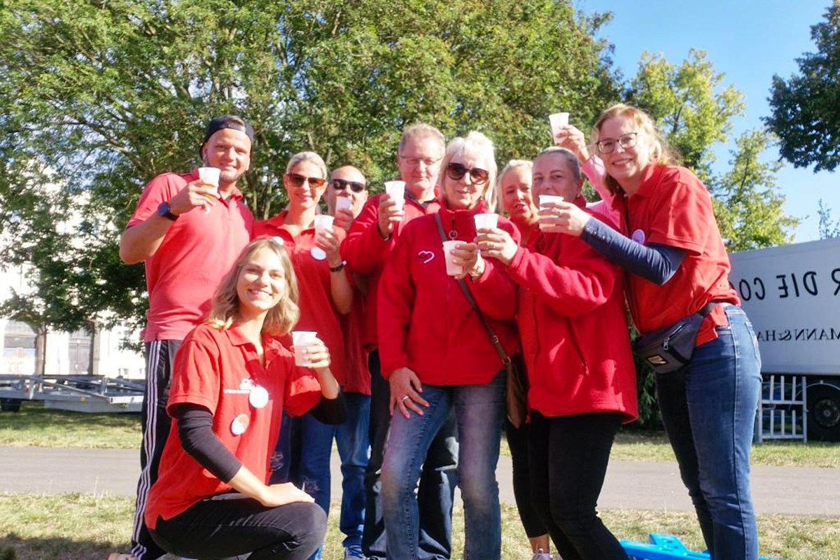 Gruppe von Menschen in roter Kleidung hält Becher und lächelt in die Kamera