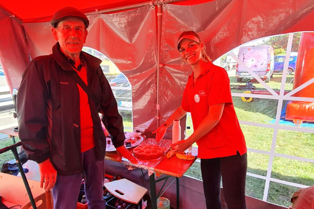 Zwei Personen bei einer Veranstaltung der AWO in einem roten Zelt.