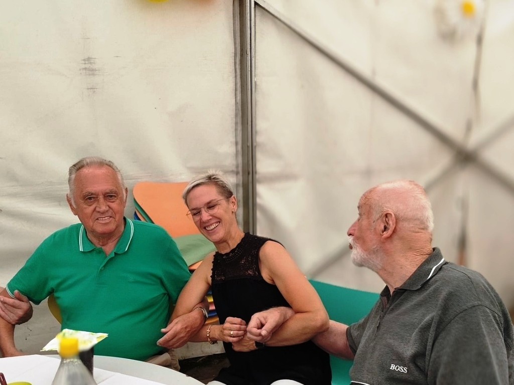 Drei Menschen sitzen zusammen an einem Tisch und halten sich an den Händen.