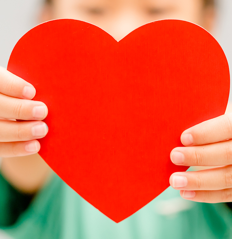 Person hält rotes Herz aus Papier in den Händen