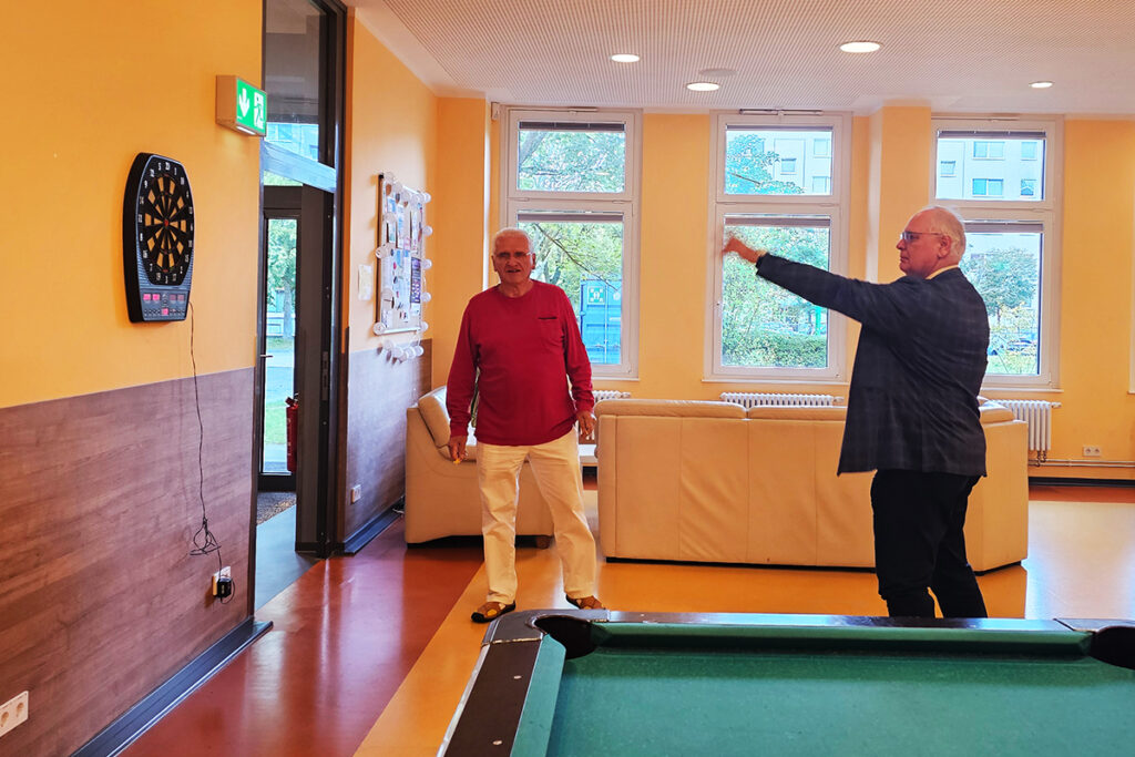 Zwei M&auml;nner spielen Darts in einem Gemeinschaftsraum.