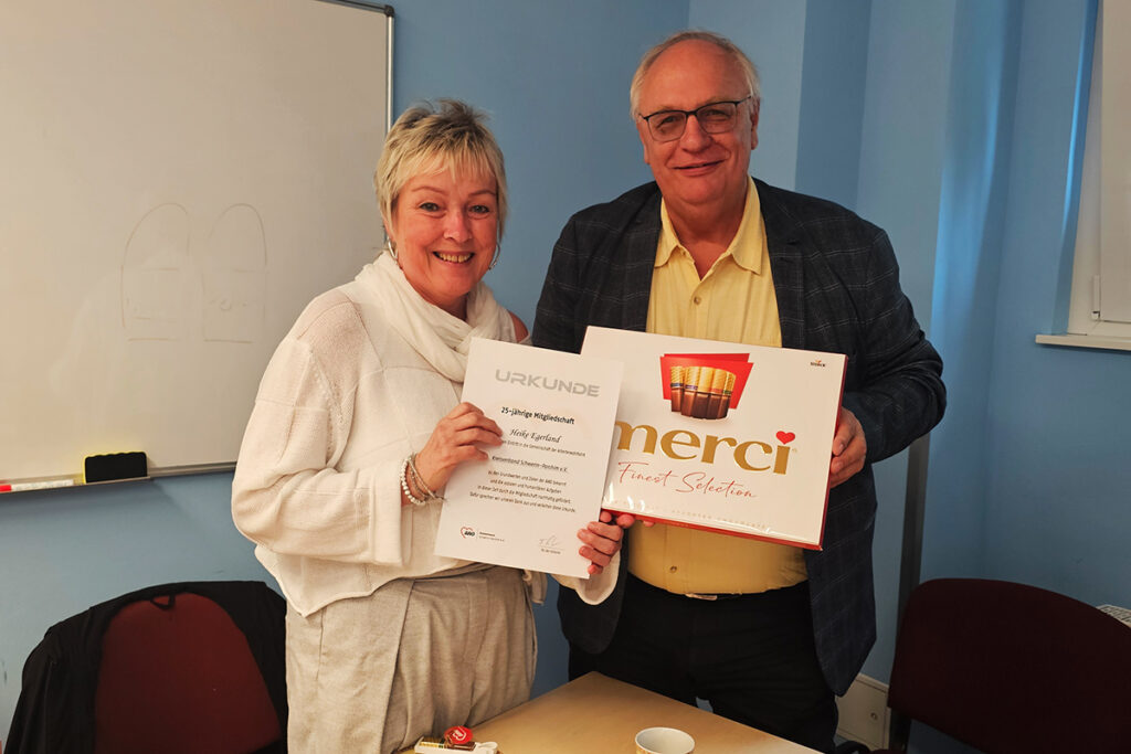 Eine Frau und ein Mann halten eine Urkunde und eine Merci-Pralinenschachtel.