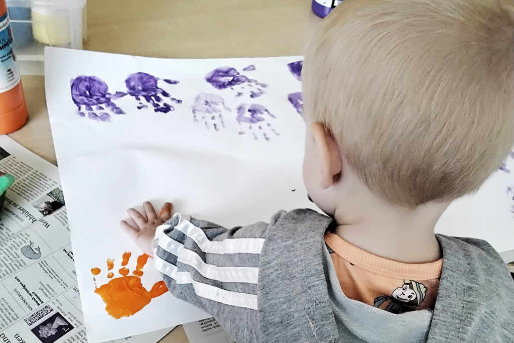 Ein kleines Kind malt mit Handabdr&uuml;cken auf einem Blatt Papier.