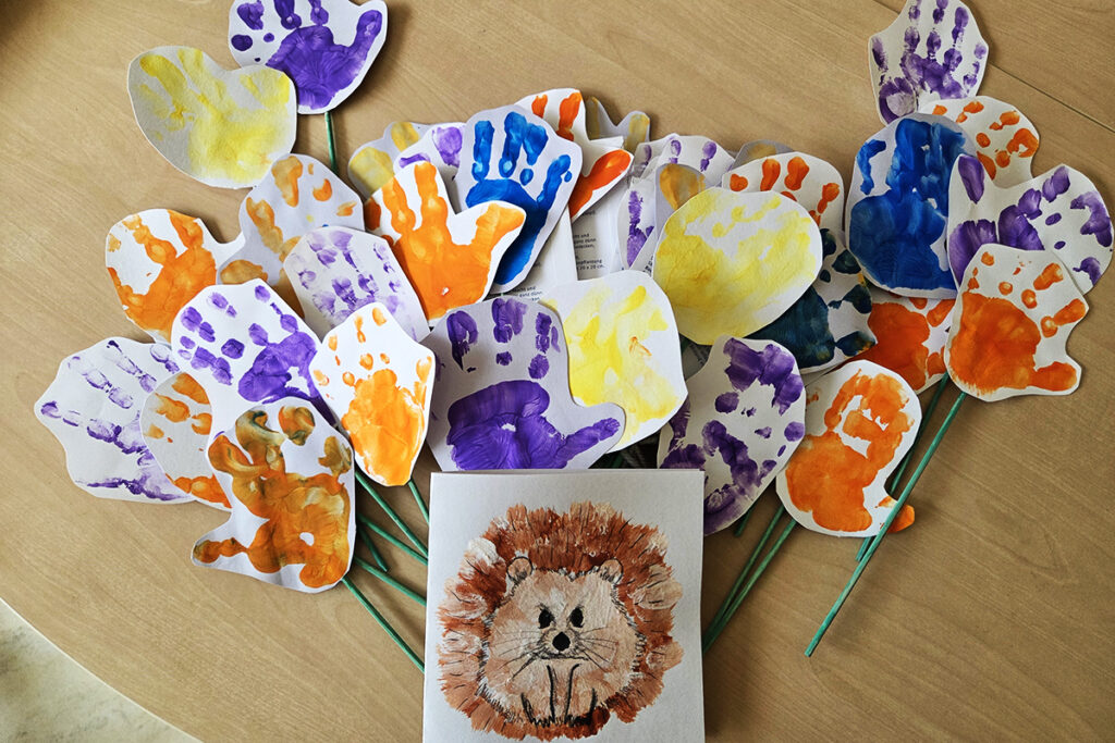 Eine Sammlung von bunten Handabdr&uuml;cken und eine L&ouml;wenzeichnung auf einem Tisch.
