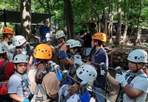 Eine Gruppe von Kindern mit Helmen und Kletterausrüstung in einer Waldumgebung.