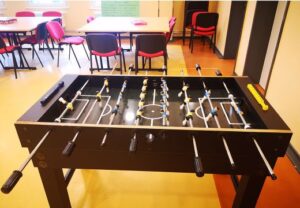 Ein Kicker-Tisch in einem Raum mit roten Stühlen und Tischen.