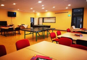 Ein Gemeinschaftsraum mit Tischtennisplatte und roten Stühlen.