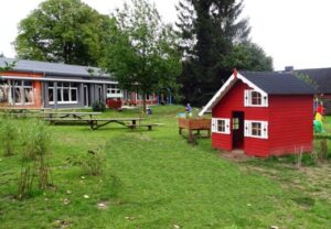 Spielplatz mit einer kleinen roten Spielhütte und einem Gebäude im Hintergrund