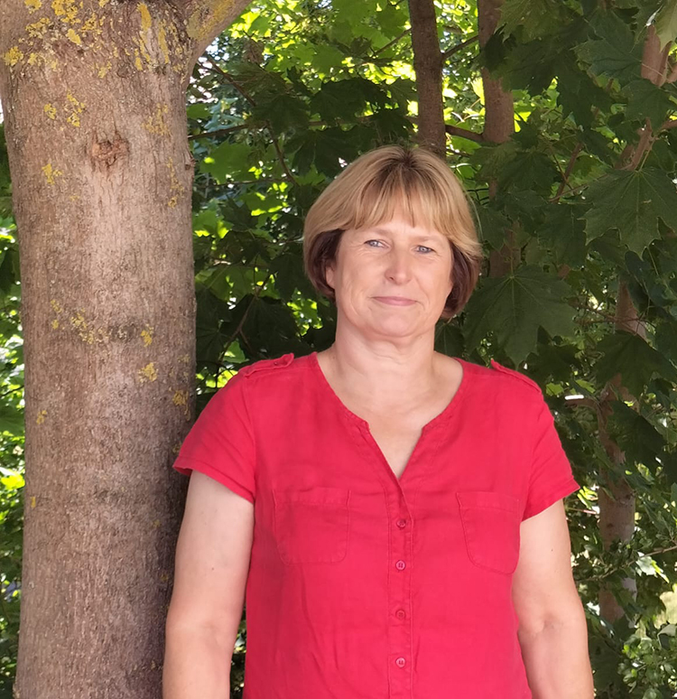 Frau in rotem Hemd steht neben einem Baum