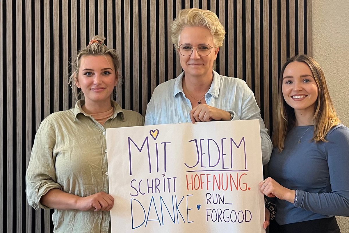 Drei Personen halten ein Plakat mit der Aufschrift: 'Mit jedem Schritt Hoffnung, Danke.'