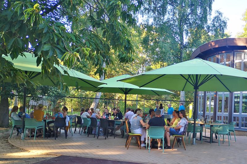 Menschen sitzen an Tischen unter Sonnenschirmen im Freien