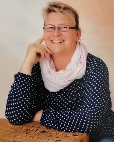 Porträtfoto einer lächelnden Frau mit Brille, Polka-Dot-Bluse und Schal