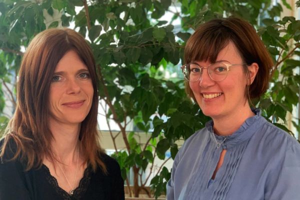 Zwei Frauen stehen lächelnd vor einer Pflanze.