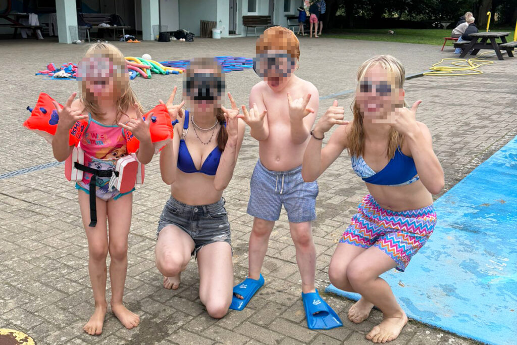 Kinder und Jugendliche in Badebekleidung vor einem Schwimmbad.