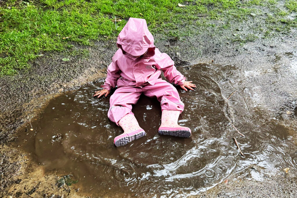 Ein Kind in rosa Regenkleidung sitzt in einer Pf&uuml;tze.