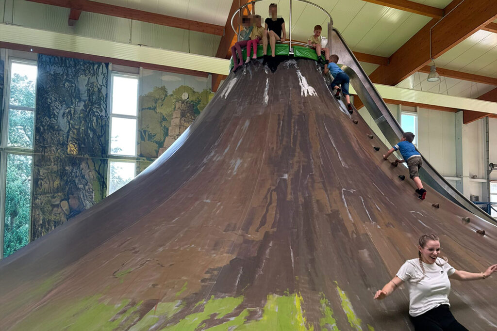 Ein gro&szlig;er Kletterkegel in einer Indoor-Spielhalle mit mehreren Kindern und einem Erwachsenen auf der Kletterstruktur.