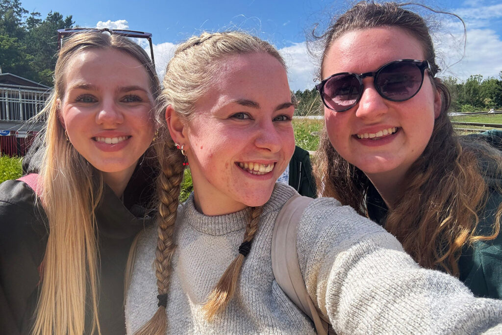 Drei junge Frauen l&auml;cheln in die Kamera, ein sonniger Tag im Freien.