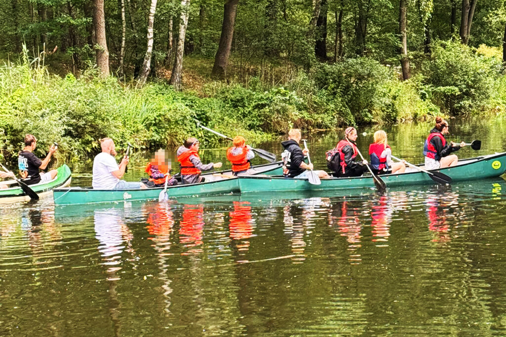 Gruppe von Menschen paddelt in einem Kanu auf einem Fluss.