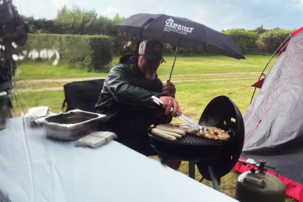 Person grillt im Freien bei Regen unter einem Regenschirm