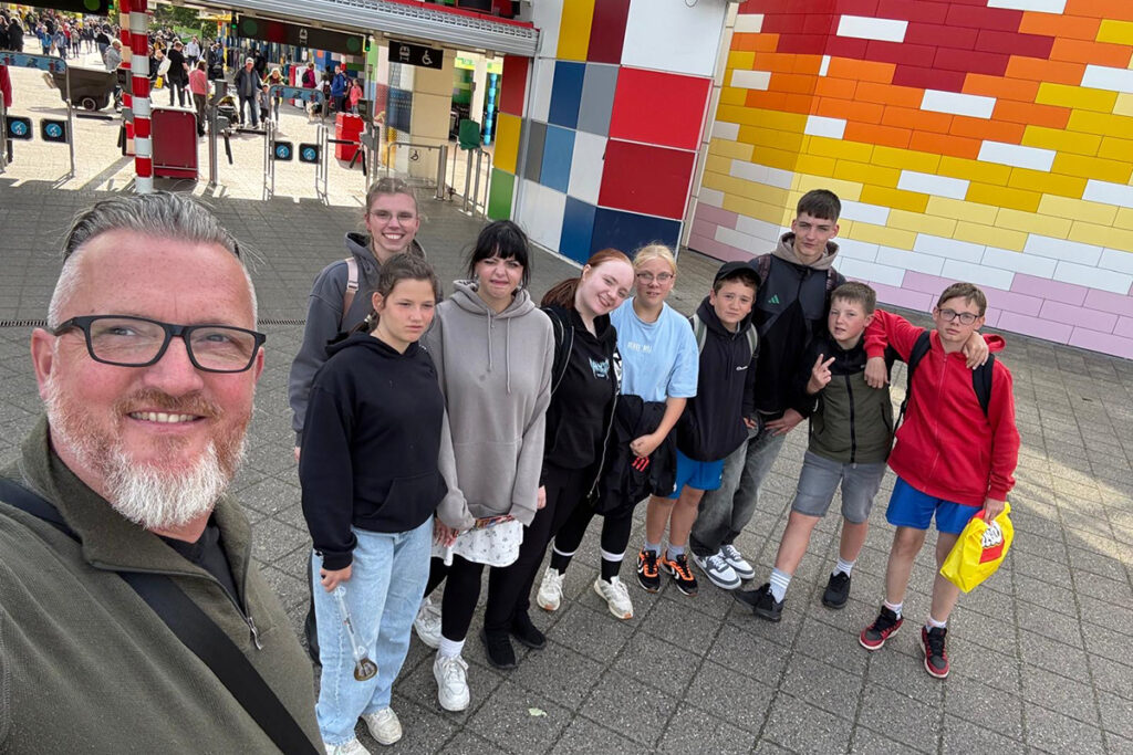 Eine Gruppe von Menschen steht vor einem Eingang mit einem bunten Wandmuster.