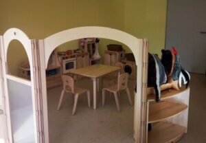 Innenansicht eines Kinderspielbereichs mit Holzmöbeln und Spielzeugküche.