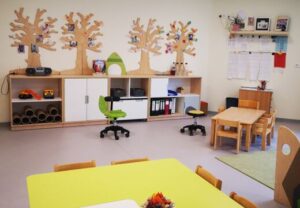 Innenansicht eines hellen Klassenzimmers oder Kindergartenzimmers mit Holzdekoration und Sitzbereich.