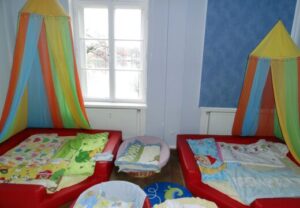 Kinderzimmer mit bunten Stoffbahnen über zwei roten Polsterbetten