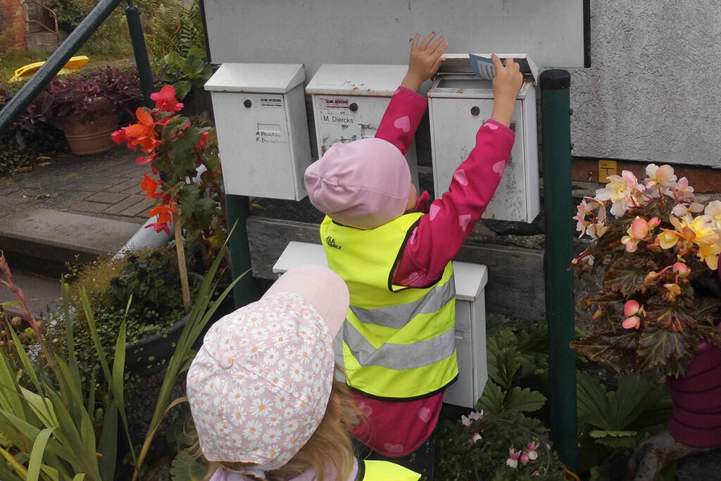 Zwei Kinder, die Post in einen Briefkasten einwerfen.