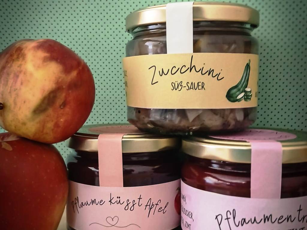 Drei Gläser mit Etiketten und ein Apfel daneben.