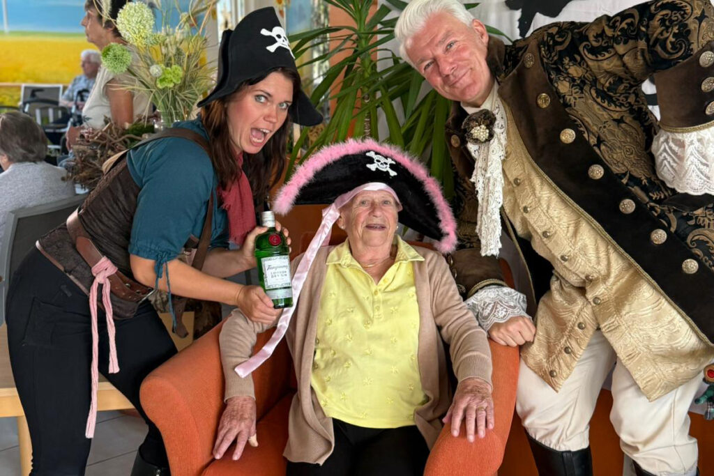 Zwei verkleidete Personen posieren mit &auml;lterer Dame in einem Sessel.