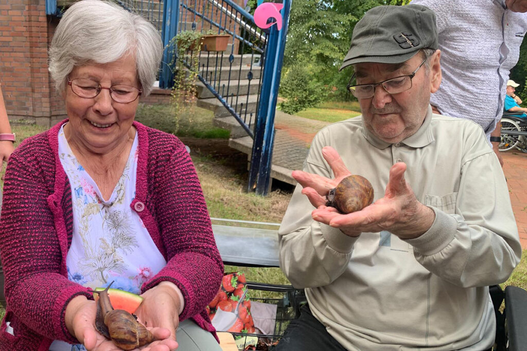 Zwei &auml;ltere Personen halten jeweils eine gro&szlig;e Schnecke in den H&auml;nden.