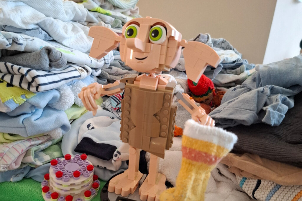 Ein Lego-Modell des Hauselfen Dobby aus der Harry-Potter-Serie steht neben einem Stapel Kinderkleidung.