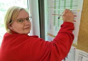 Person in roter Jacke schreibt an einer Wandtafel