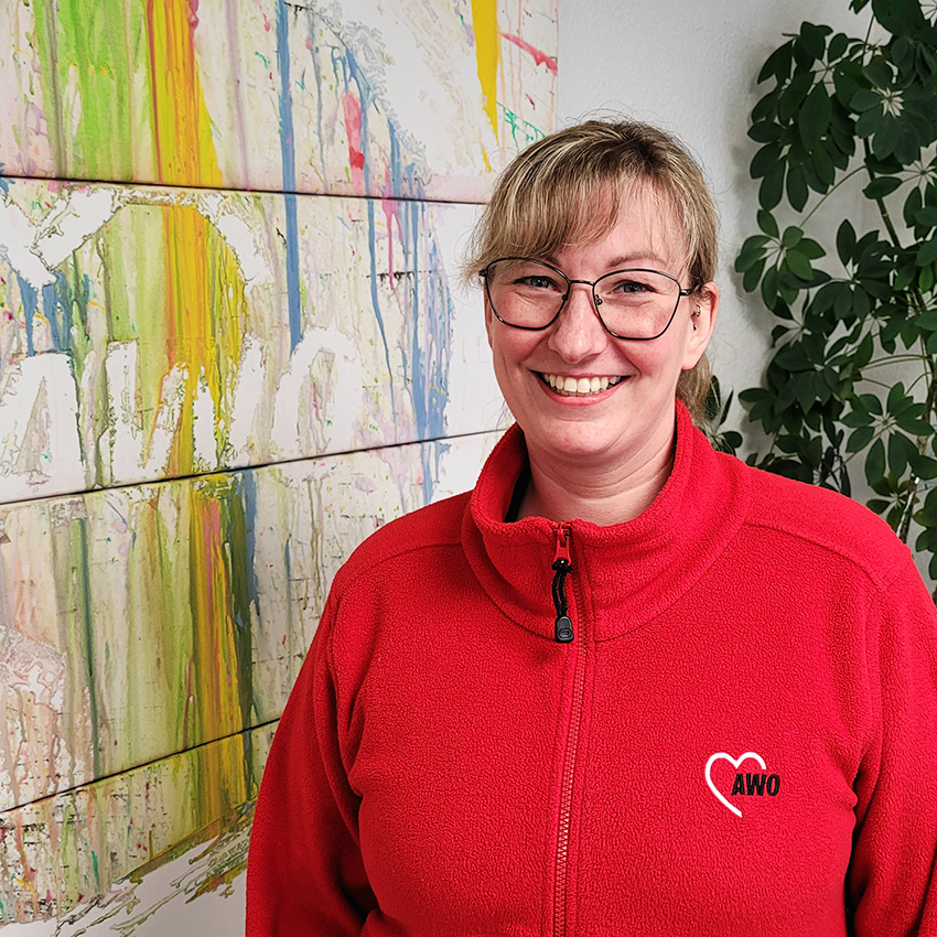 Frau in roter AWO-Jacke vor einem bunten AWO-Logo