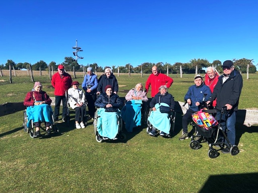 Gruppe von Menschen, darunter einige im Rollstuhl, bei einem Ausflug im Freien unter einem klaren blauen Himmel.
