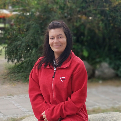 Eine Frau in einem roten Pullover sitzt draußen und lächelt.